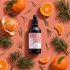 kaisa MORGENLICHT Kissen- und Raumduft, 100-ml-Sprühflasche mit Mandarinen und Nadelzweigen auf korallfarbenem Hintergrund